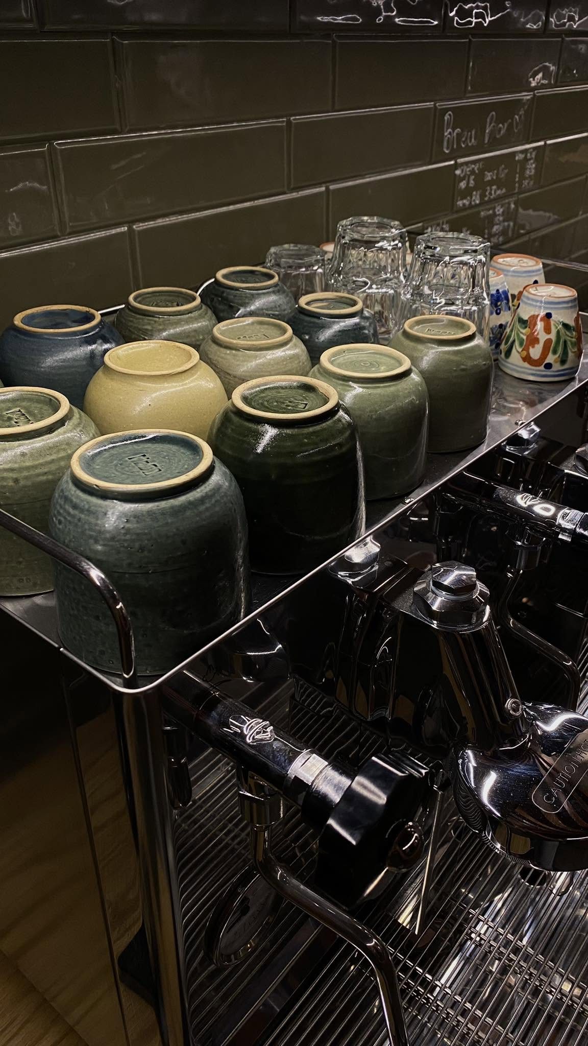 Barra de La Cuatro con jarras de cerámica verde oliva y utensilios de café