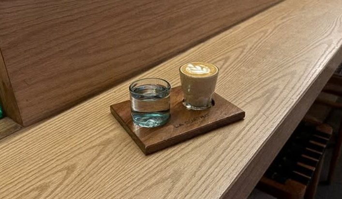 Latte con arte y vaso de agua sobre tabla de madera en la barra